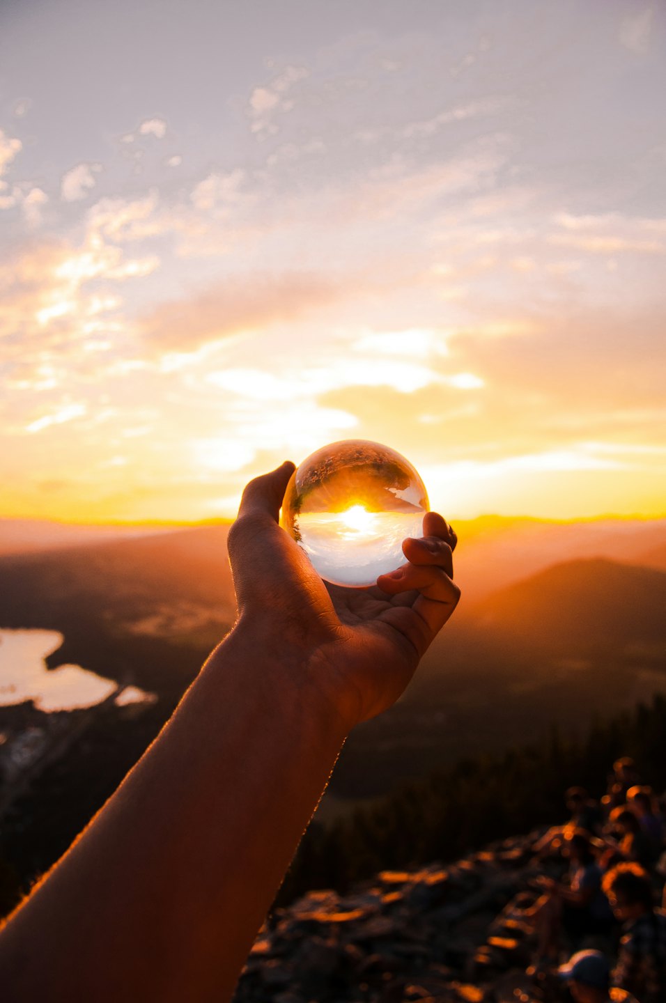 Main tenant une boule de cristal reflétant un coucher de soleil sur les montagnes.