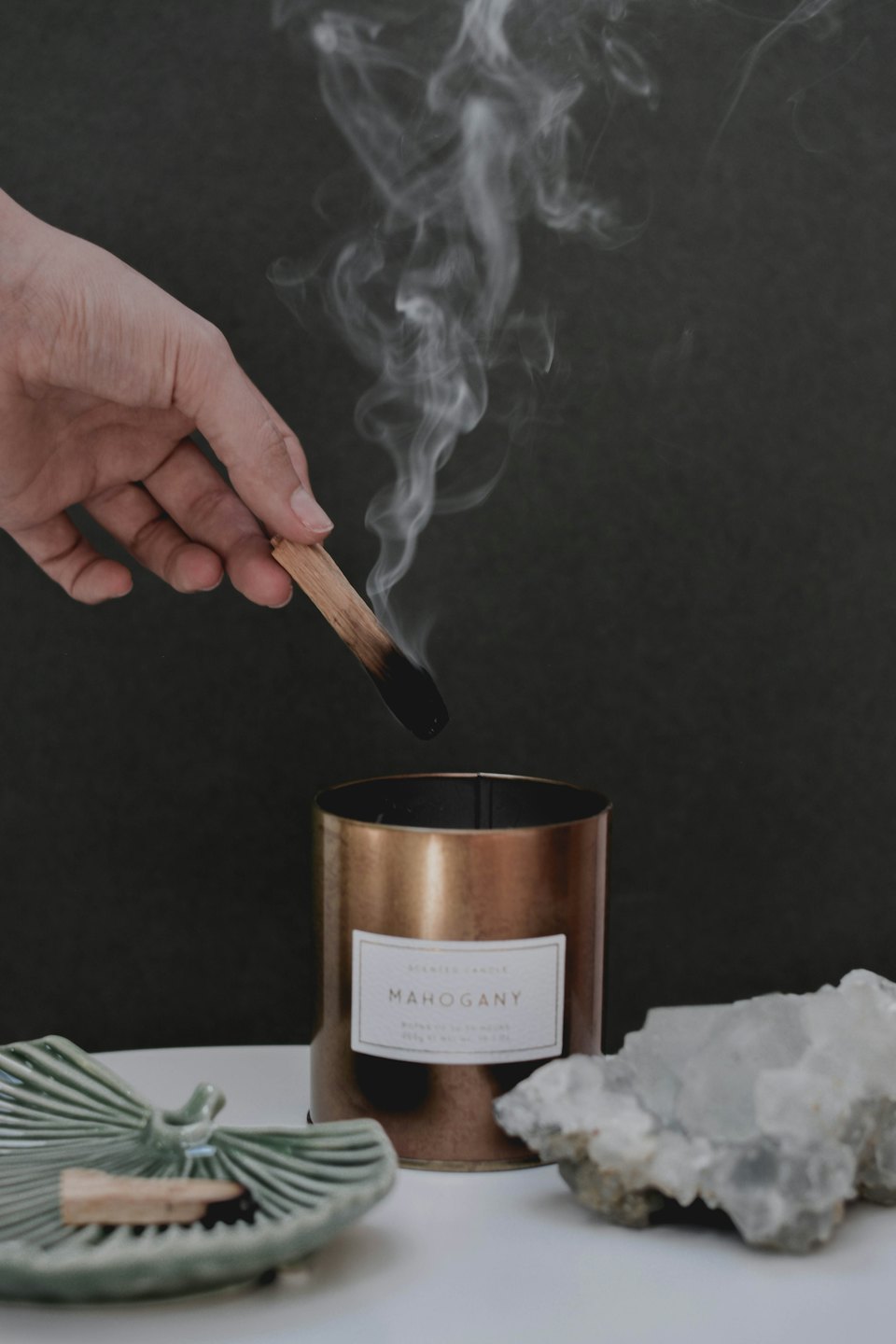 Main tenant un bâton de palo santo fumant au-dessus d'une bougie parfumée à l'acajou.